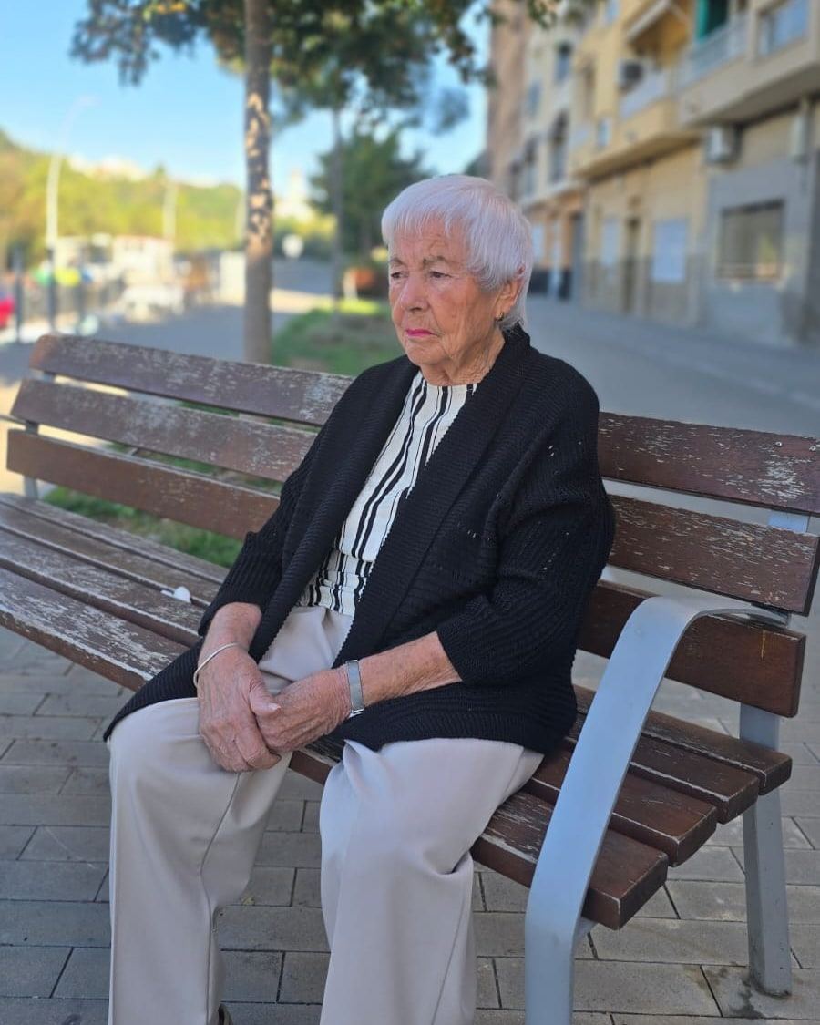 Senyora gran asseguda sola en un banc del carrer, amb la mirada perduda